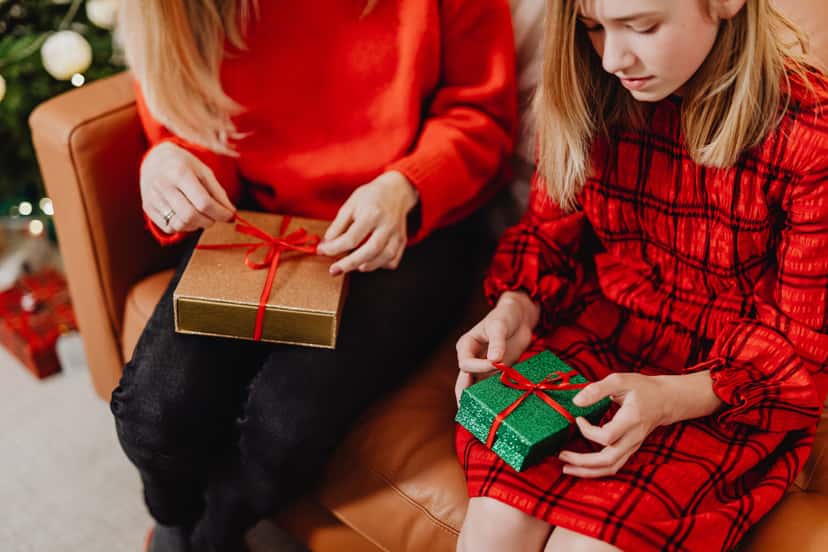 A mother and daughter opening small wrapped Christmas gifts together by the tree