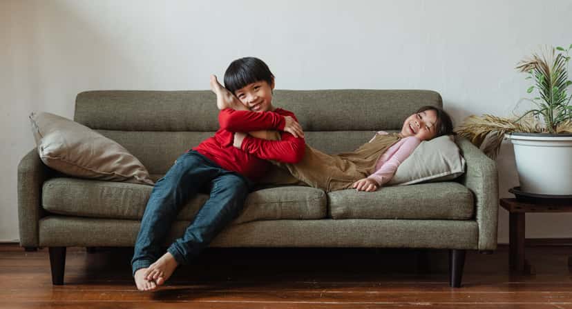 Two young siblings laughing and hugging together on a living room sofa
